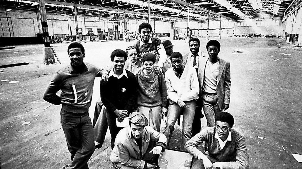 Black and white image of eleven people in an large empty warehouse