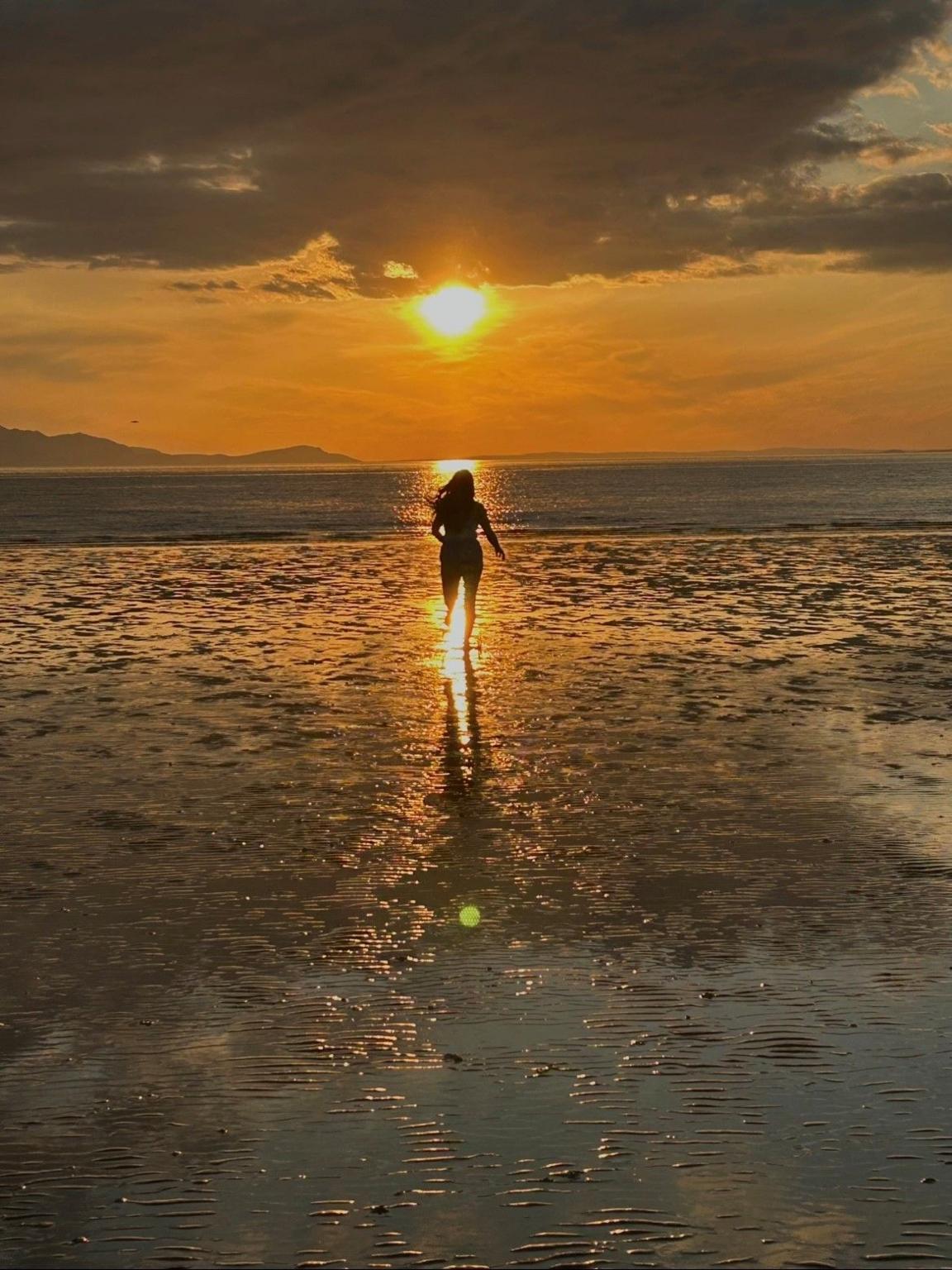 A person runs into the sea as the sun sets