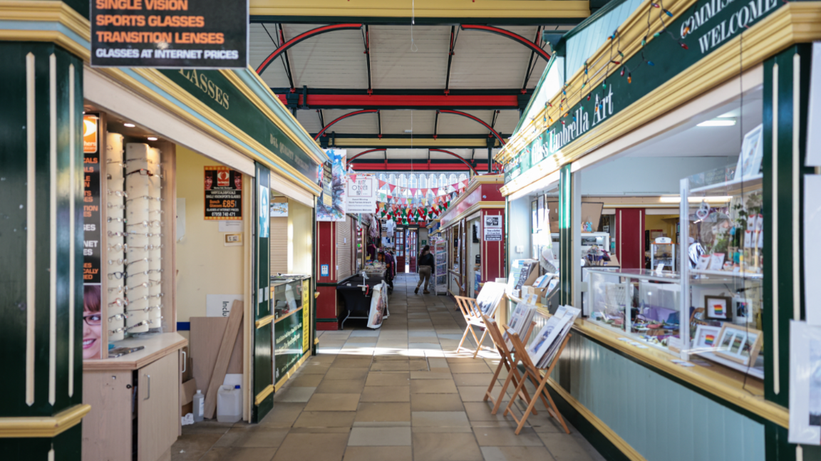 The inside of the market with work displayed outside the art shop inside the covered market