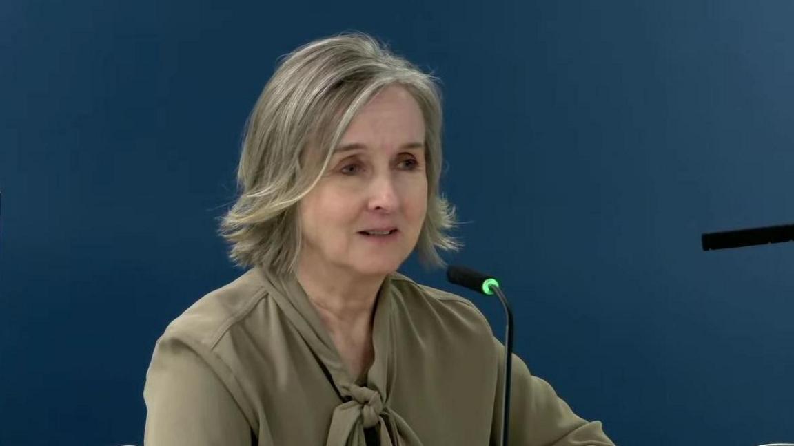 Briege Donaghy, chief executive of the RQIA, speaking at the UK Covid-19 inquiry. She has shoulder length dark grey hair and is wearing a khaki coloured blouse