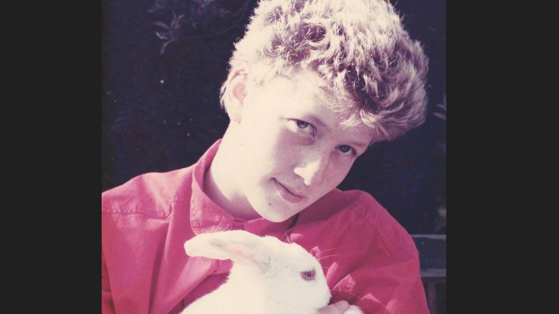 Photograph of 18-year-old Sarah Beckett, who lost her life in the Manchester Air Disaster. The teenager, wearing a red shirt, is holding a white rabbit as she looks at the camera.