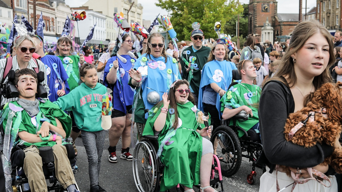 People, some in wheelchairs, dressed in colourful clothing and carrying flags.