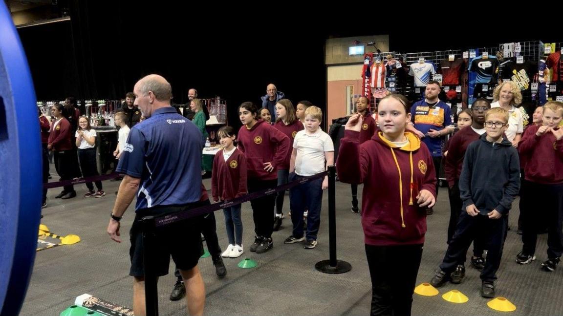 Children lining up and holding darts ready to throw them on a board.