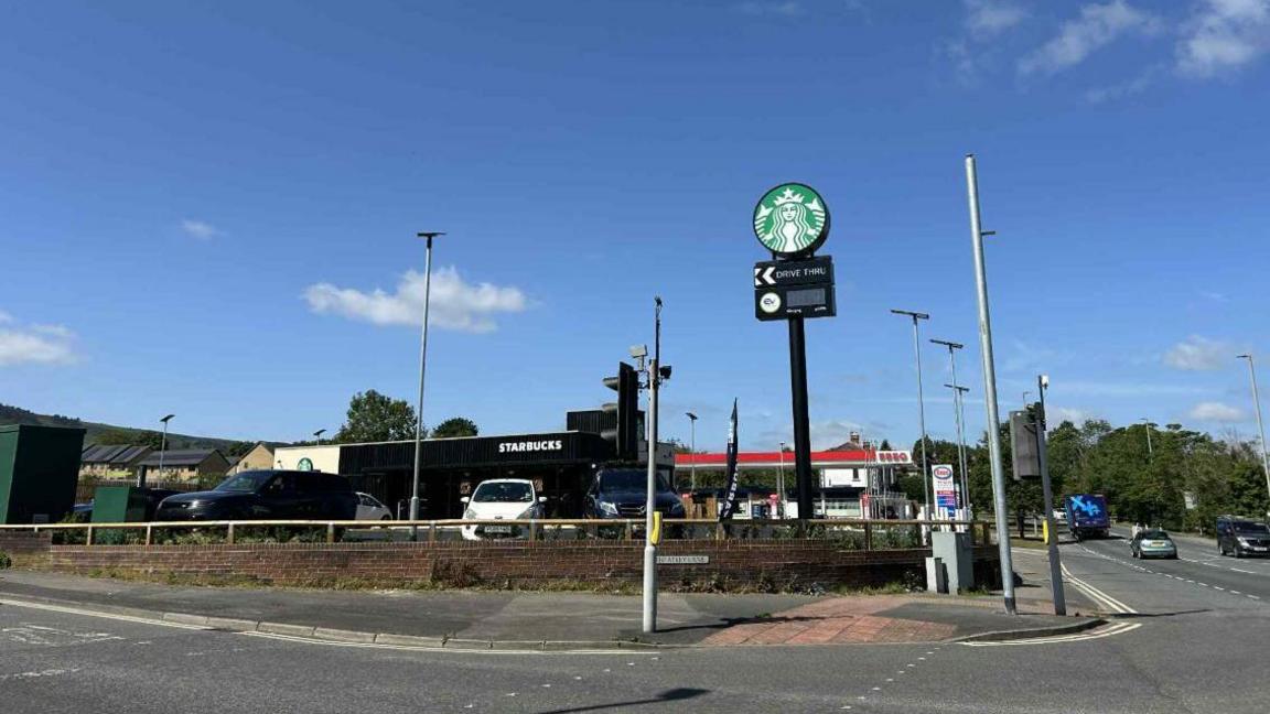 An image of a Starbucks drive-thru on the corner of a main road with a tall sign outside.