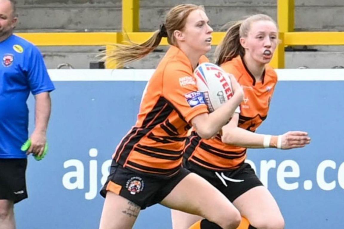 Courtney pictured running on a rugby pitch while holding a rugby ball. A teammate can be seen in the background.