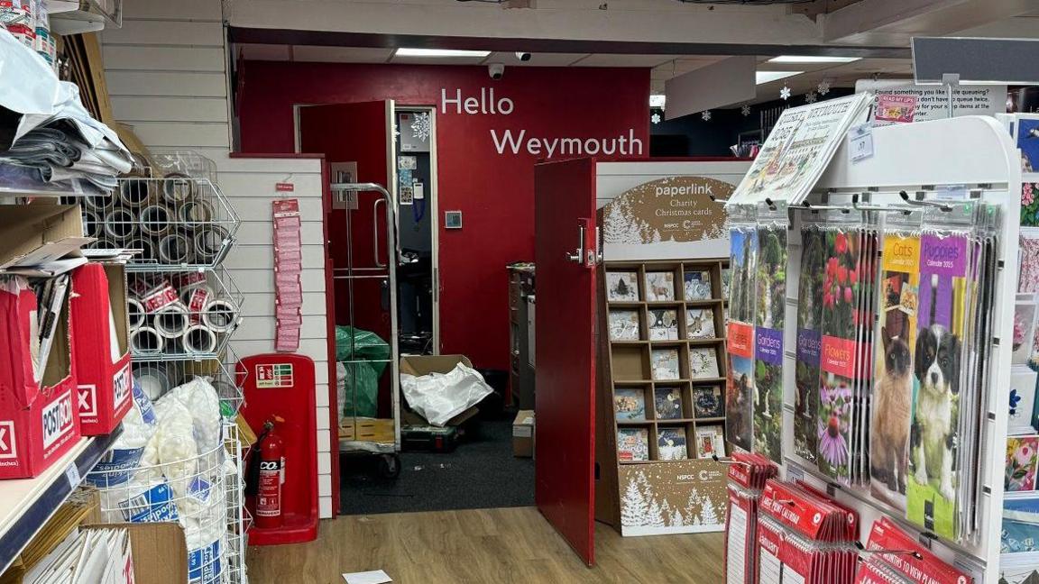 The inside of a post office shop with the door to the back room open with parcels littering the floor.