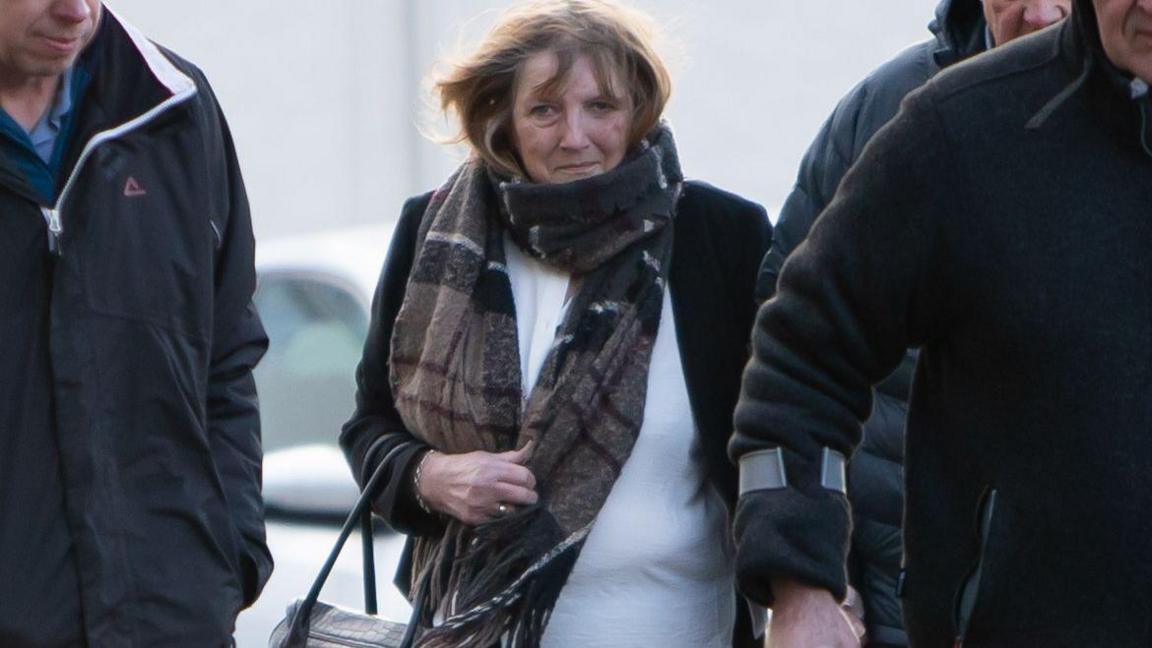 Bridget Curtis who has fair hair and is wearing a white top, black jacket and black-and-brown scarf.