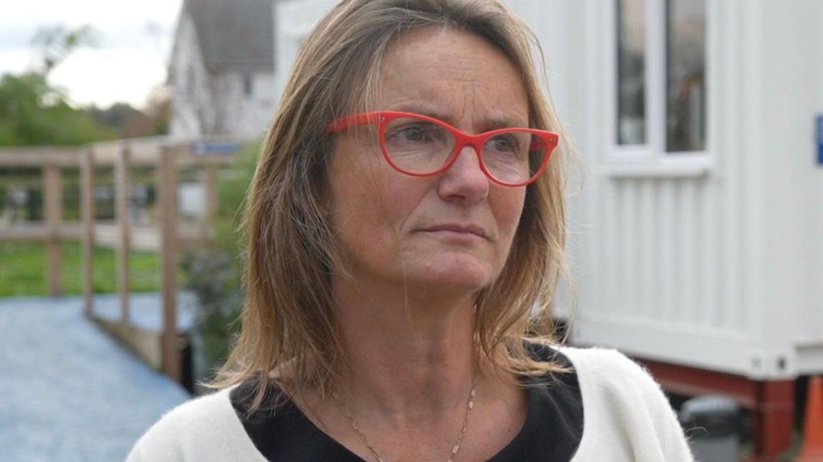 Jade Martin standing outside a shipping container being used as a temporary reception building at Debenham Veterinary Practice. She has shoulder-length brown hair and glasses. She is wearing a cream jumper over a black top.