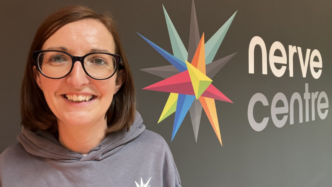 Shows a woman in a grey hoodie and dark-rimmed glasses smiling beside a logo for the nerve centre