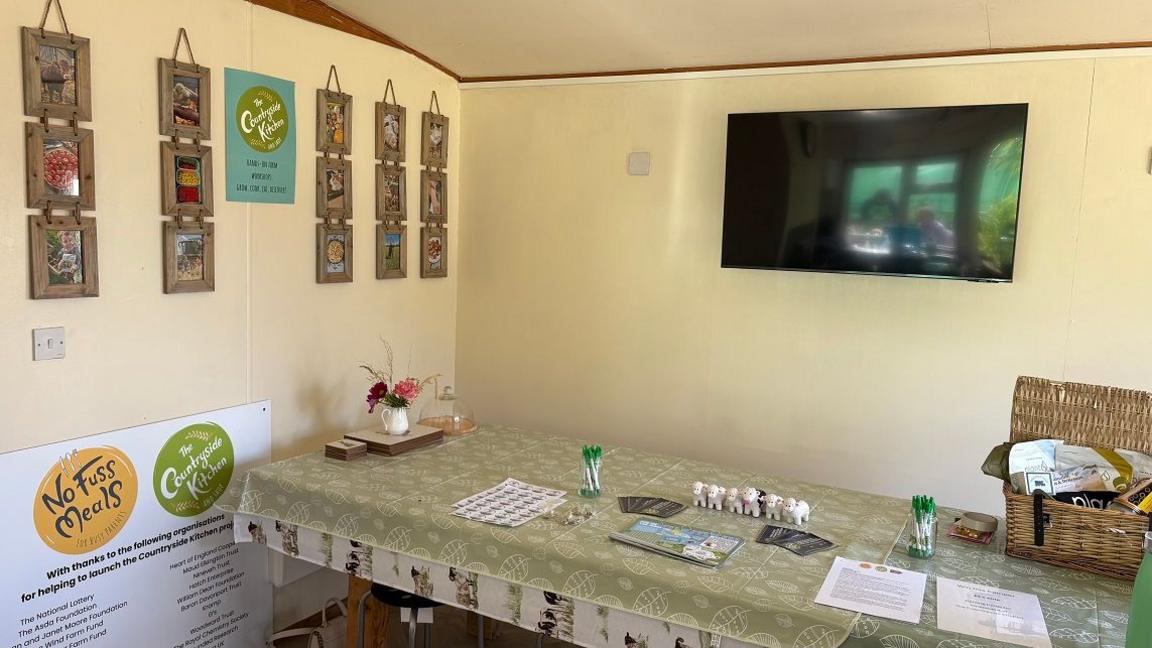 The interior of the classroom showing pictures on walls, a TV screen and a table, on which various objects are placed.