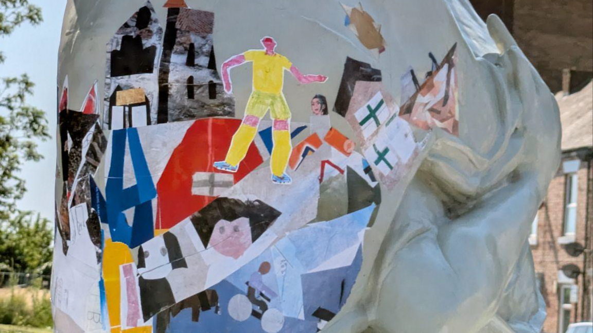 A close up of the artwork by the community on the sculpture. It looks like a scrapbook page with various colourful cut outs in varying shapes.
