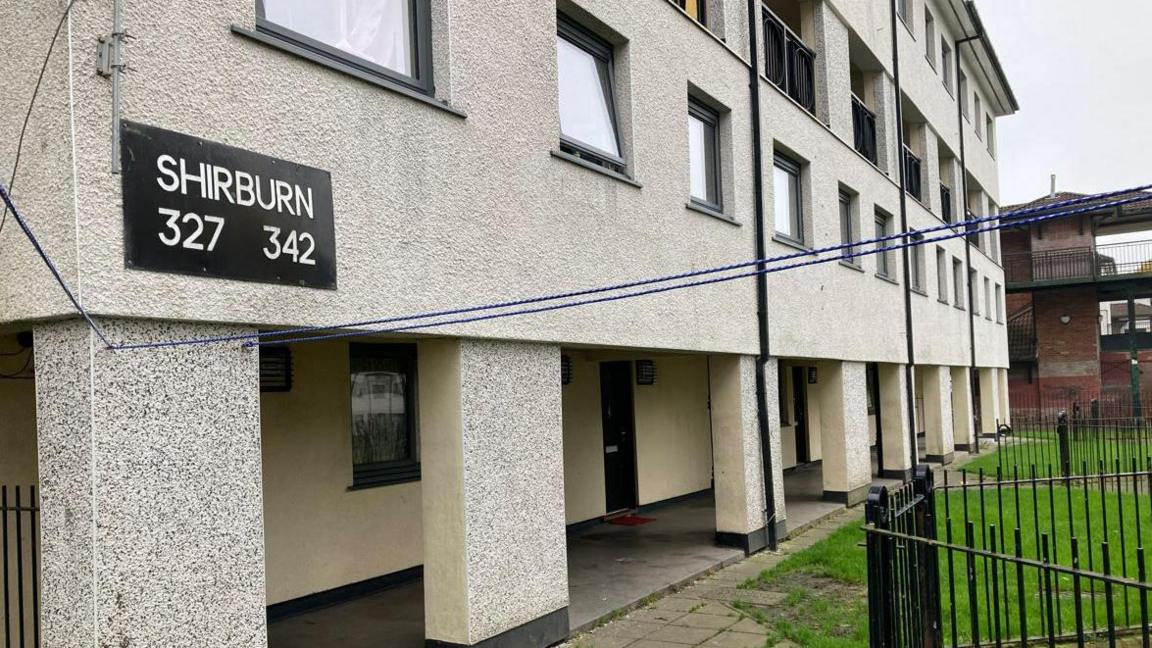 A block of flats, with a black sign on the left hand corner of the wall which reads 'Shirburn 327 342'