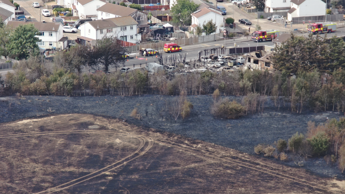 Blackened field and burnt buildings next to urban area