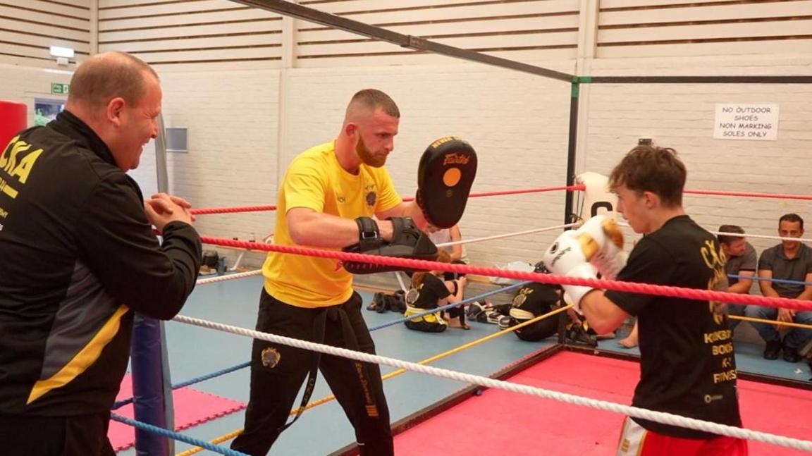 Leon Dunnett in the ring, coaching a younger fighter while his father looks on. 