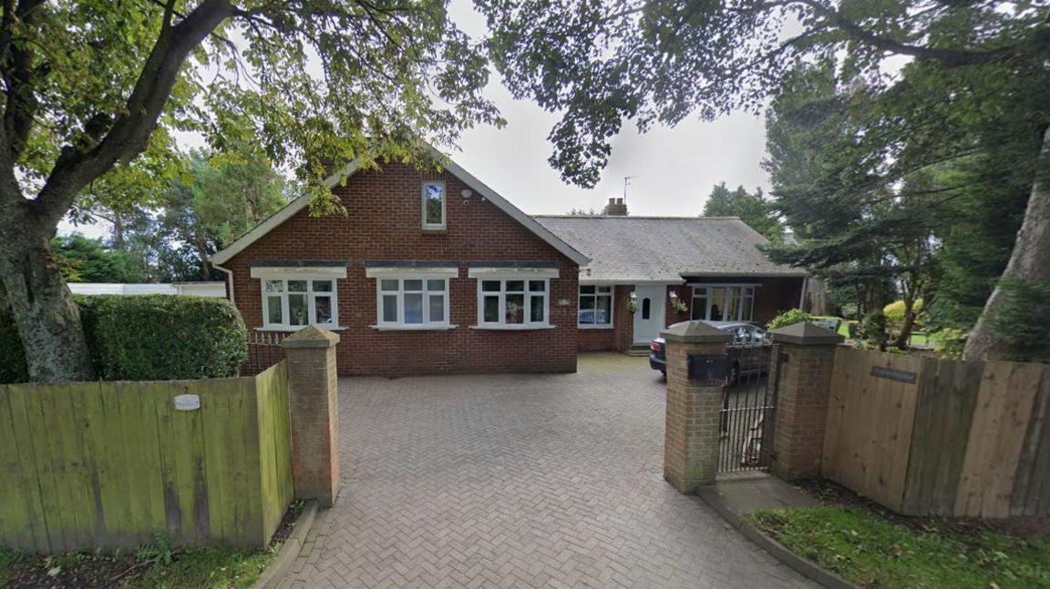 The red brick house on Black Boy Road. The property is a large bungalow witha  garage. It has a large driveway and has a wooden fence around its garden.