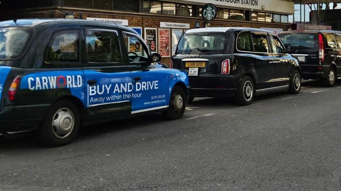 A row of black taxis outside a train station