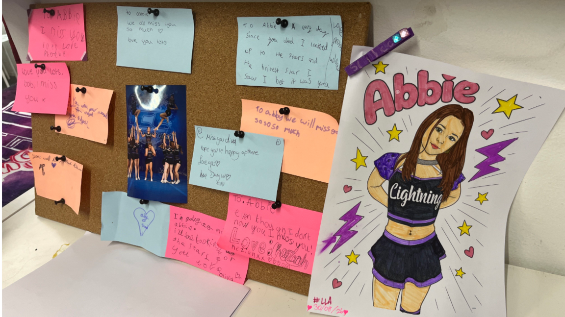 A noticeboard at Swindon Lightning Cheerleading Club covered in pink, orange and blue post-it notes with messages written in memory of Abbie, alongside a picture drawn of Abbie wearing the Lightning Cheerleading kit.