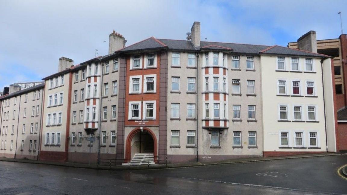 The exterior of the Lord Street flats, an aged block of flats, which has an archway entrance with steps leading into it on the corner of two roads.