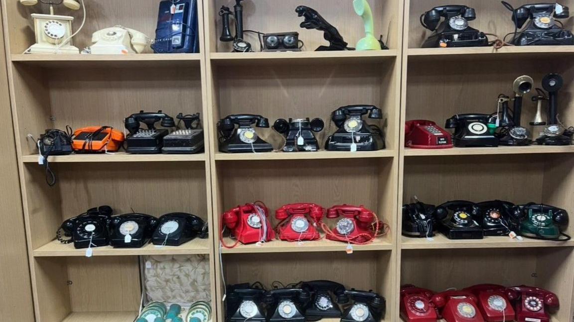 Phones are on shelves over five levels, with at least eight phones each on most levels. Many of them are red or black.