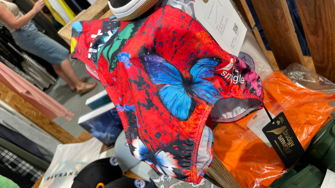 A pair of red swimming trunks with butterflies on them. Other items can be seen in the background.