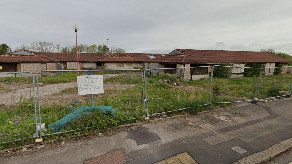 The buildings of Combe House, in a state of disrepair and gated off by steel fencing