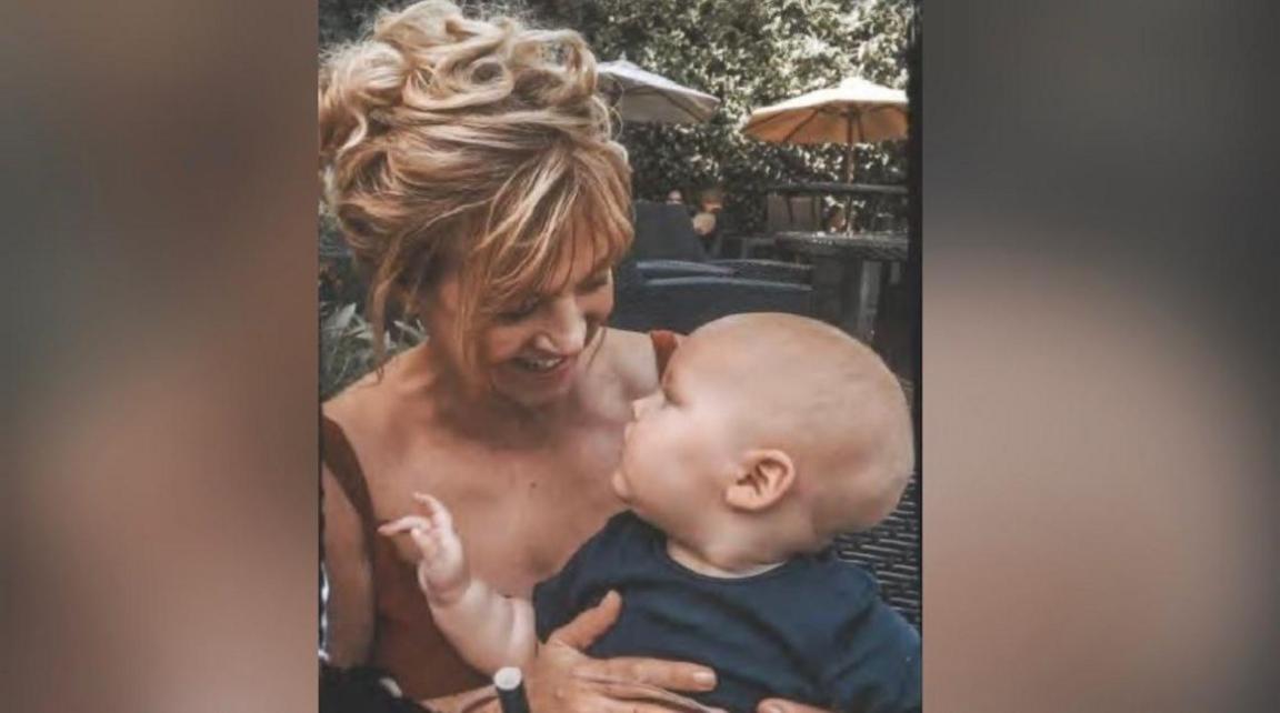 A woman with long blond hair holds a baby 