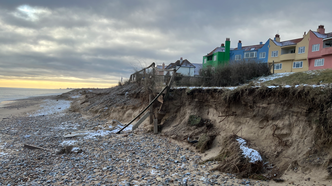 An image taken on a beach showing the sea and a row of rainbow-coloured houses perched close to a cliff edge in Thorpeness.