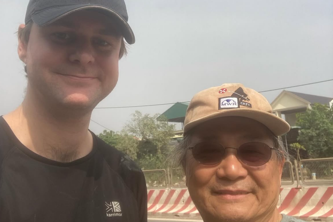 Cameron Taylor wears a black tshirt and baseball cap and stands next to a man in a tan baseball cap.