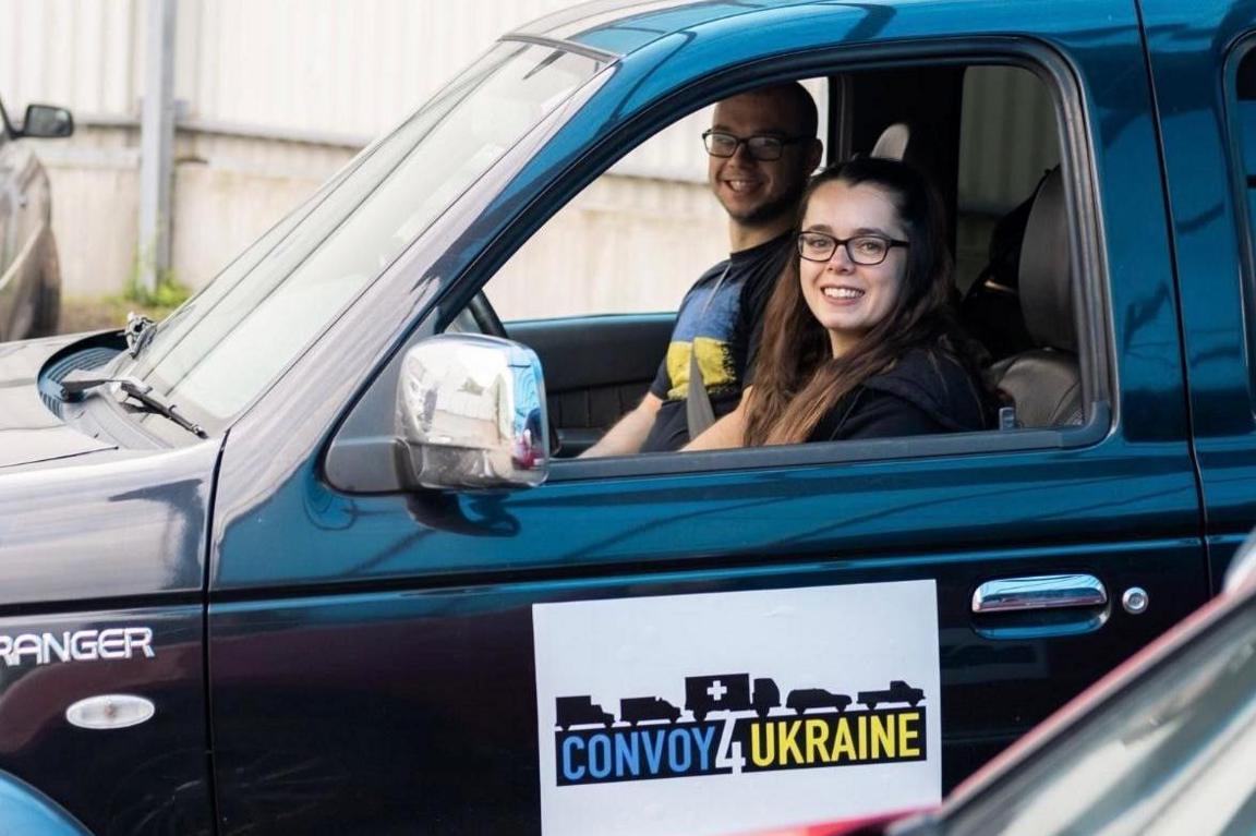 Kayleigh Jones looking out of the window of a dark-coloured vehicle, with the words Convoy 4 Ukraine on the door and her partner, Josh Katihrob, sitting in the driver's seat