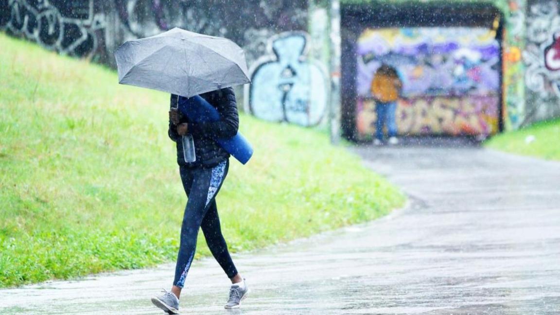 A woman in a sports kits walking under an umbrella in heavy ran