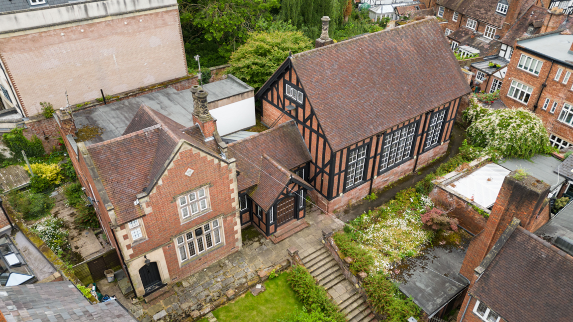 An aerial view of a red brick building with large windows, part of the building has exposed dark timber as part of its construction