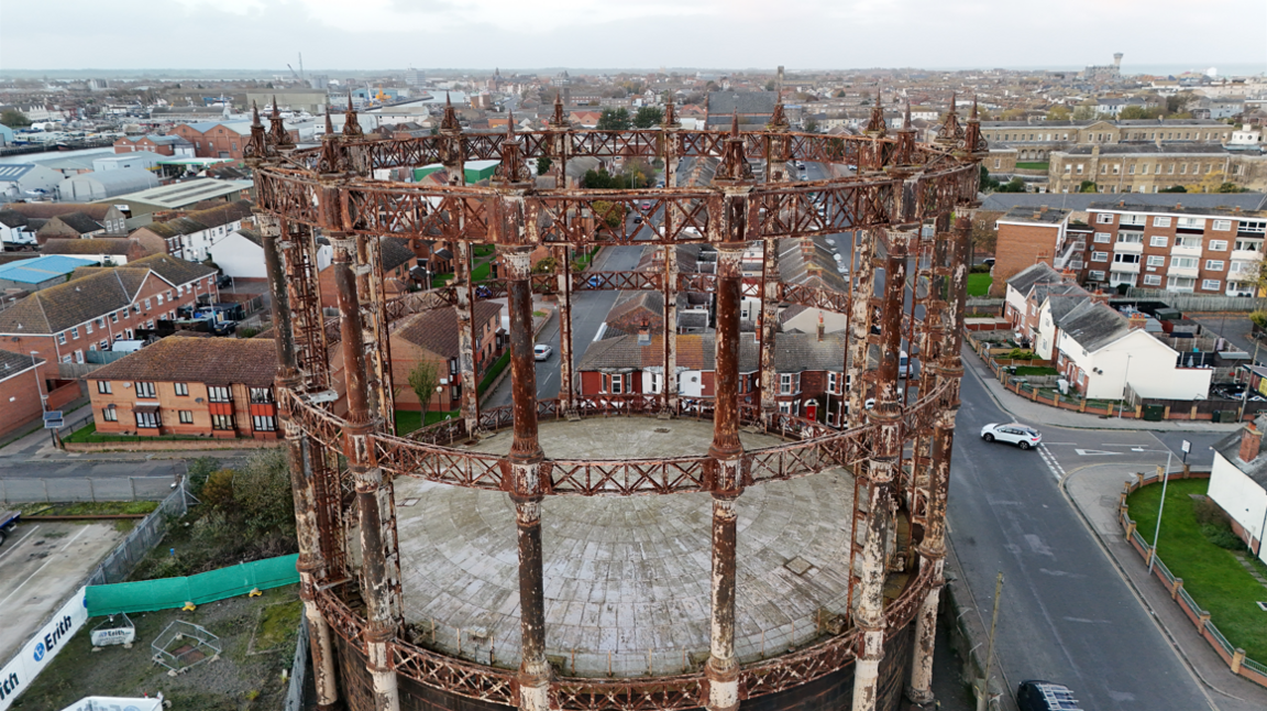 Drone image shows rusting gasometer structure rising over nearby homes and businesses.
