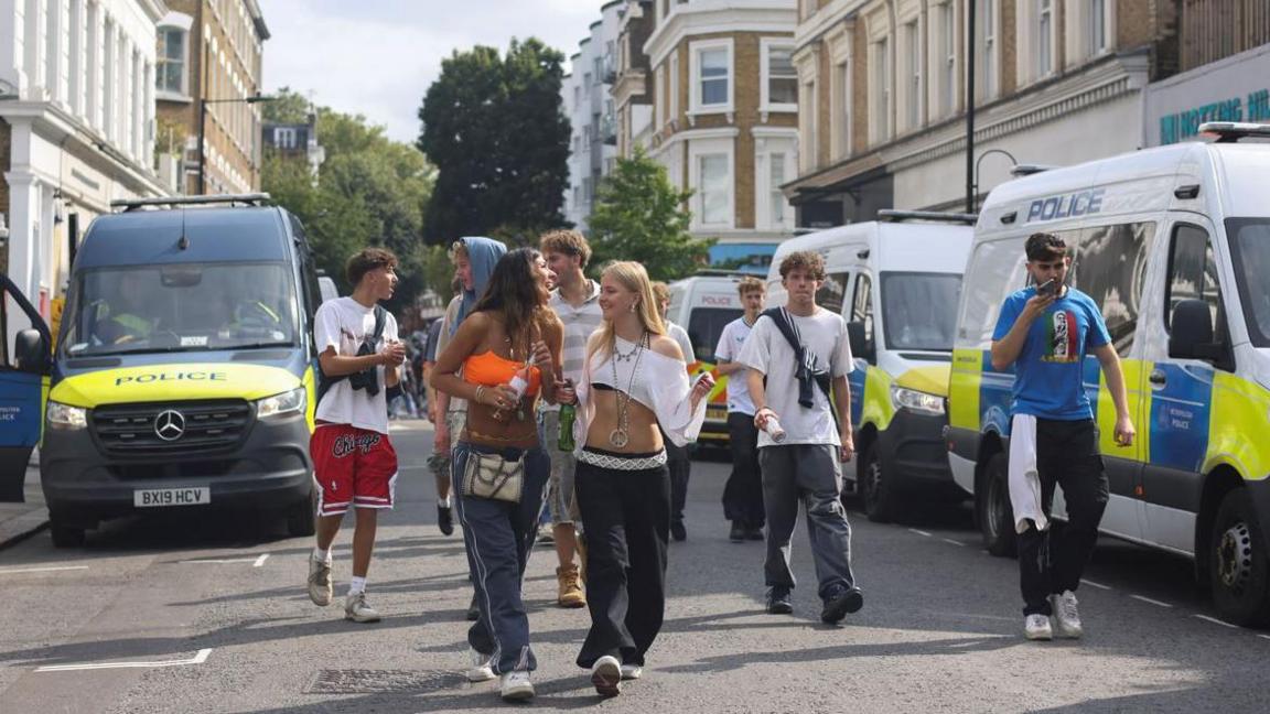 Image of a group of teens walking down the road in between two police vans at Notting Hill Carnival in 2024