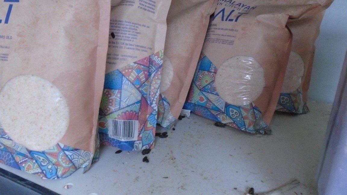 Close-up of bags of food on a dirty shelf with rat droppings around them.