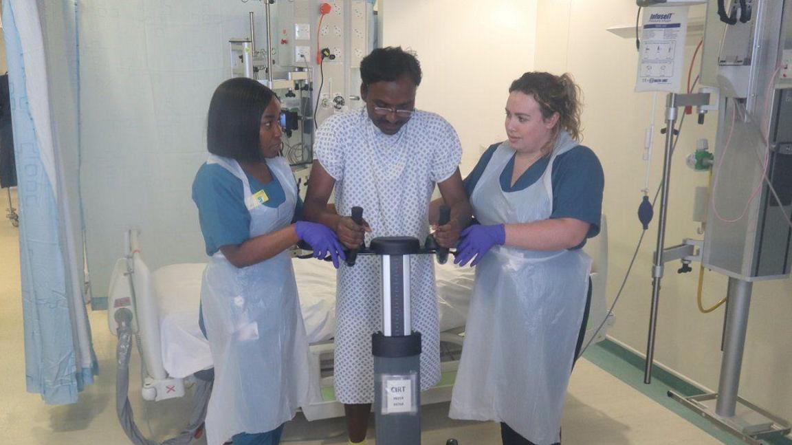 Two nurses supporting a patient in a hospital ward