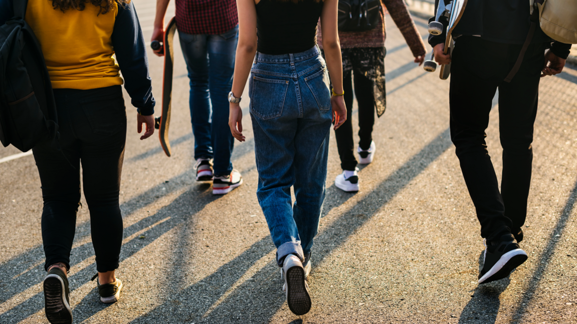 Rear view of a group of school friends walking outdoors dressed in  jeans and trainers