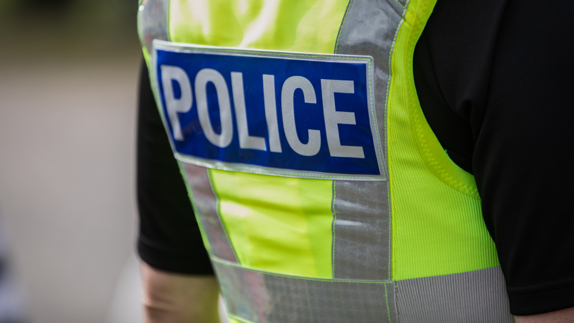 A police officer wearing a yellow high visibility vest, viewed from the back