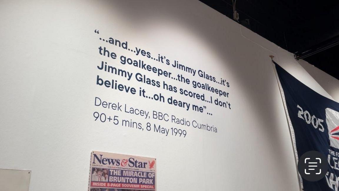 A quote from BBC Radio Cumbria's Derek Lacey from 8 May, 1999, 90 plus 5 mins into the game. It's printed on to a wall reading "and... yes... it's Jimmy Glass... it's the goalkeeper... the goalkeeper Jimmy Glass has scored... I don't believe it... oh deary me". At the bottom there is a front page from the News and Star with a headline The Miracle of Brunton Park.