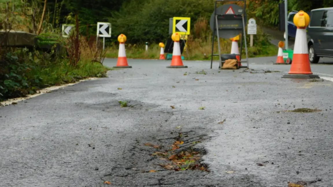 A road damaged by landslips surrounded by cones 