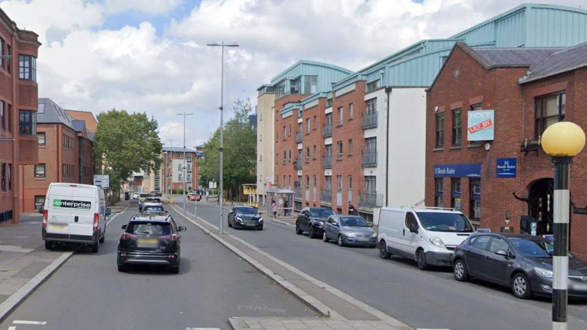 A generic image of Greyfriars Road showing cars going away from the camera. Other vehicles are parked on the opposite side of the road. Red brick buildings line each side.