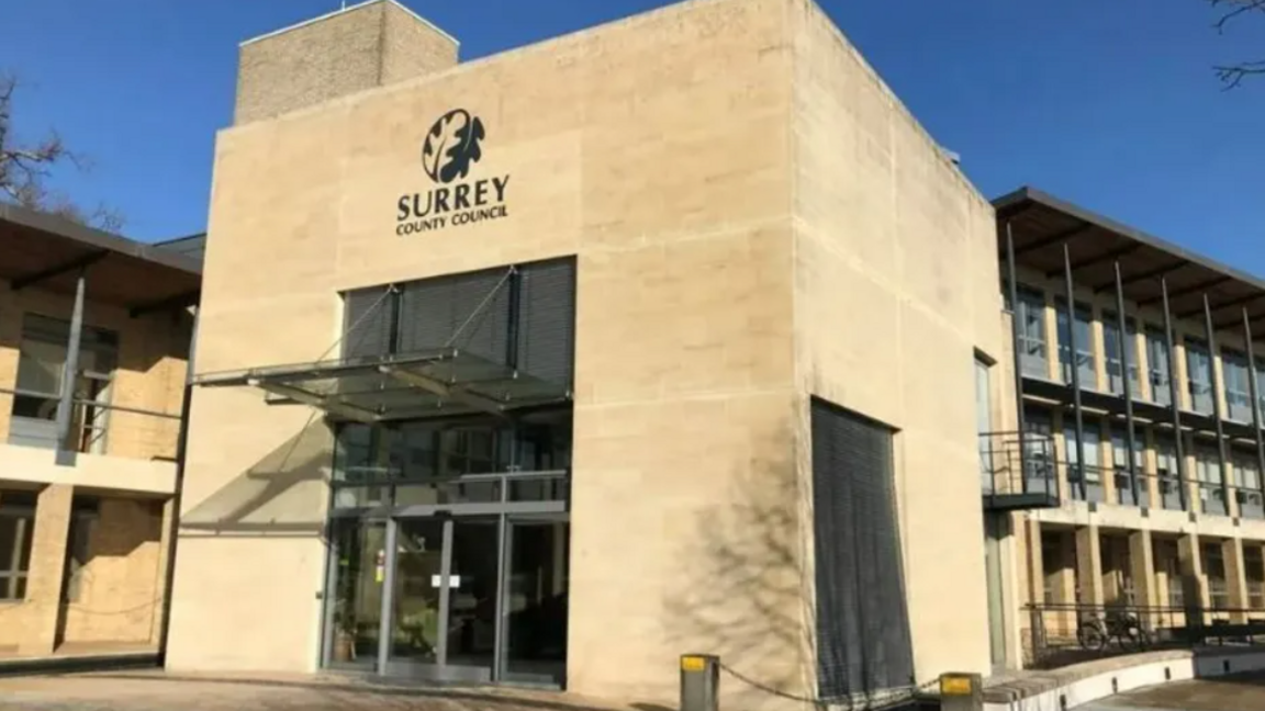 Surrey County Hall, with the name of the council inscribed on the sand coloured building, with blue sky in the background.