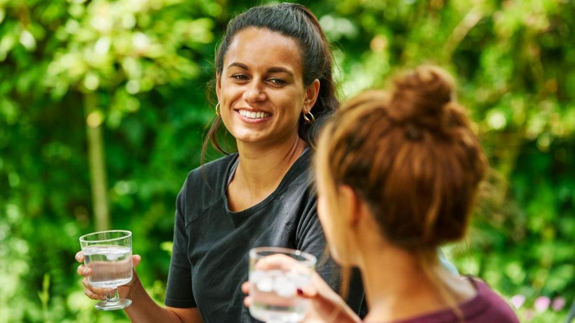 In a picture provided by the utility company two women drinking glasses of water outside