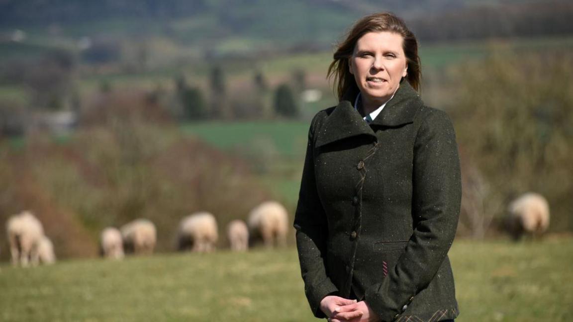 Hybu Cig Cymru chairwoman Catherine Smith standing in a field with sheep, and she is smiling at the camera