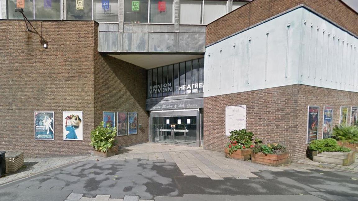 The entrance to the Wyvern theatre in Swindon - a red brick building with grey cladding and some planters outside. 1960s style.