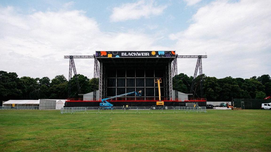 The Blackweir Live concert stage seen on a field with fencing around it. There are tents and construction equipment on either side.