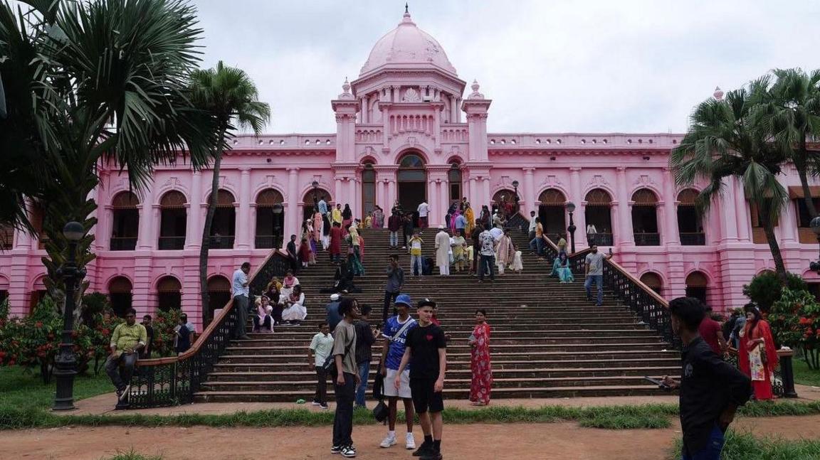 Zak Hajjaj, Abu Finiin, Kayum Miah standing outside the steps of the pink palace (Ahsan Manzil) in Dhaka, Bangladesh surrounded by people