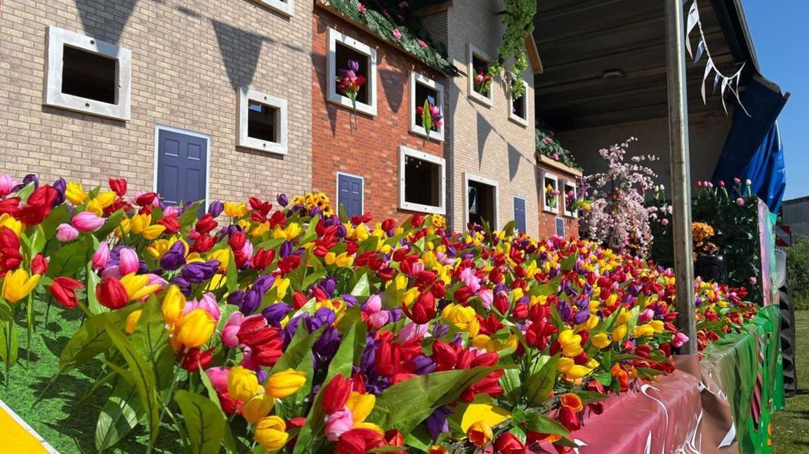 Red, yellow and purple tulips at the front of a model village, which has been created on a parade float.