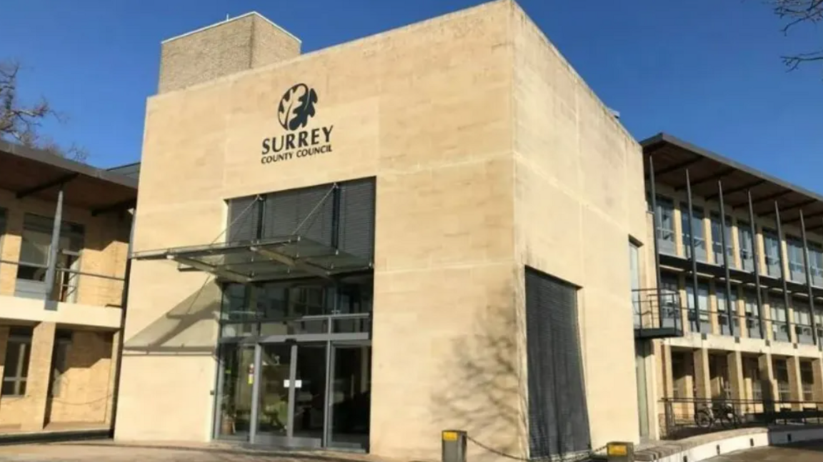 The exterior of Surrey County Hall, a pale yellow building, with steel window frames and girders in front of some of the windows