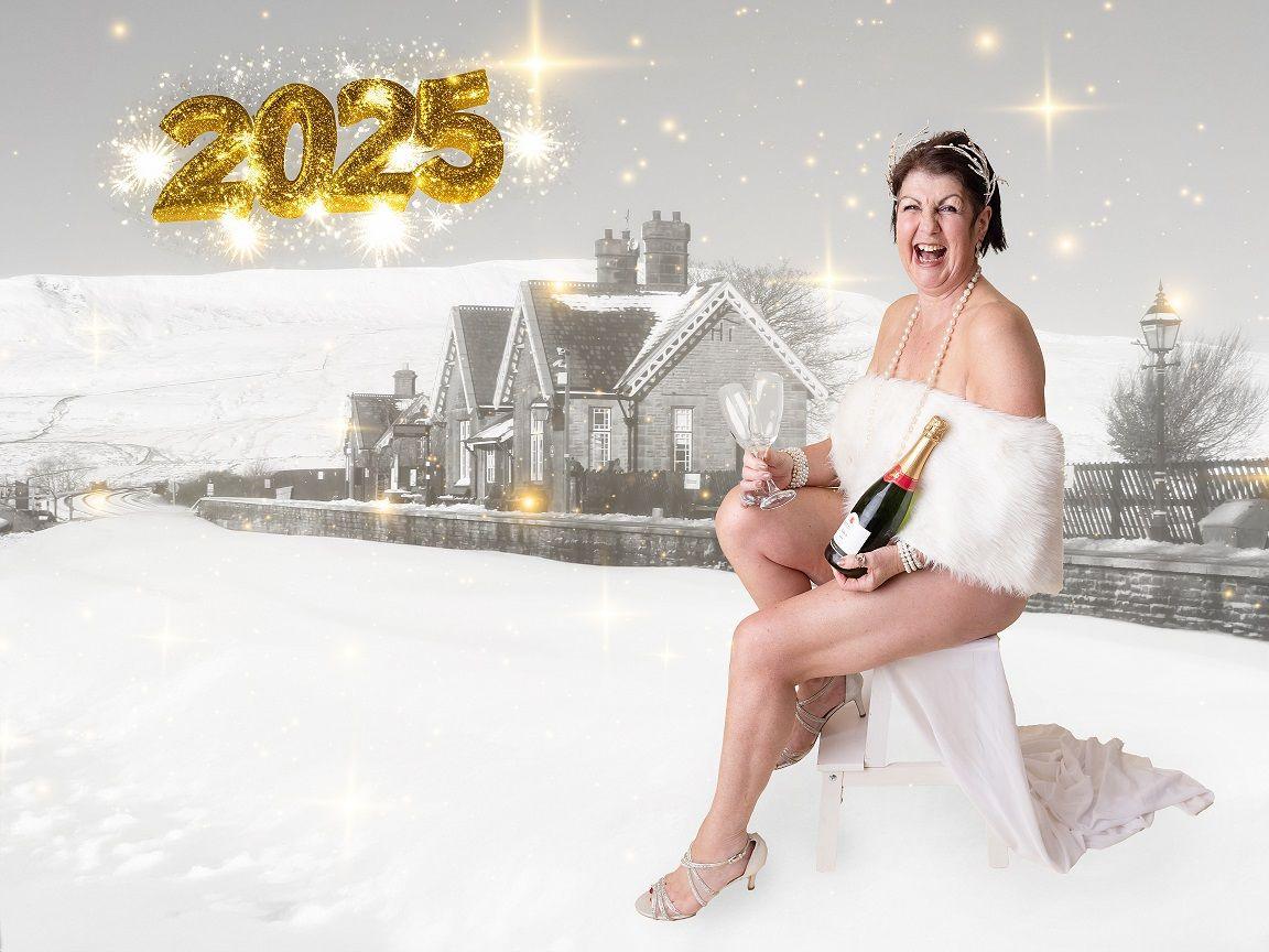 A woman with short brown hair holding a bottle of champagne and wearing a pearl necklace sitting down along a train track covered in snow. She is draped in a white fur dress, which shows her legs. 