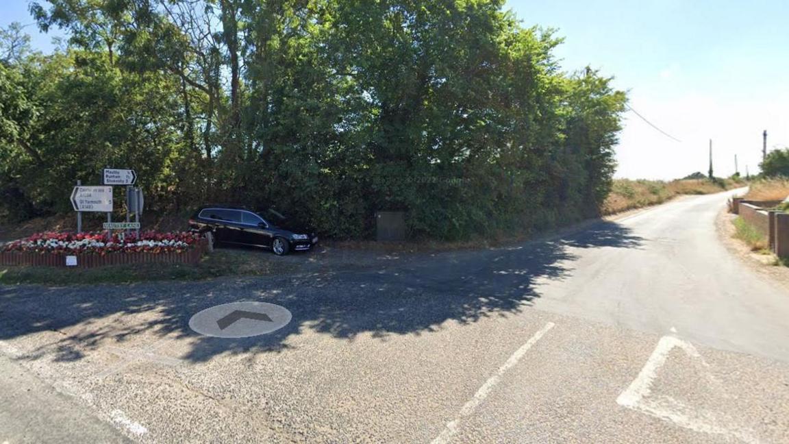 Give way road markings on a country road, with signposts and a roadsign to the left.